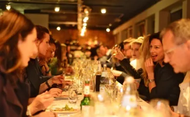 Angebote der Woche von nicko cruises Personen sitzen an einer langen Tafel und genießen ein mehrgängiges Menü bei einer Eventkreuzfahrt von nicko cruises.