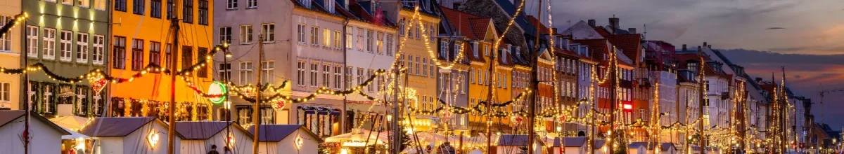 Ein Weihnachtsmarkt mit einer beleuchteten Uferpromenade und kleinen Häusern.