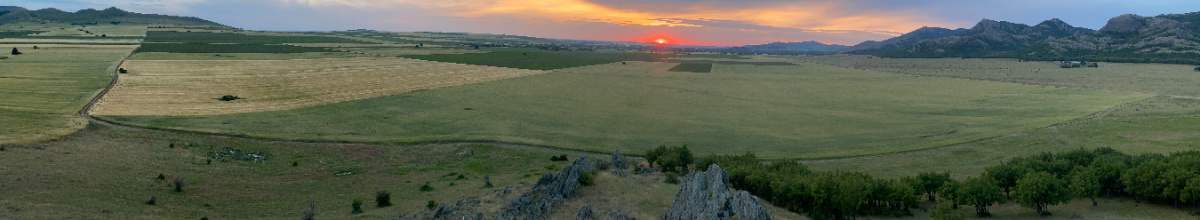 Während im Hintergrund die Sonne aufgeht, blickt man im Vordergrund über die hügelige Landschaft in Rumänien.