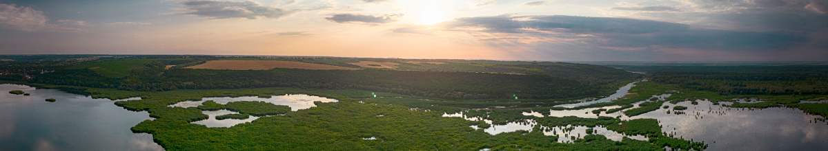 Auf dem Panoramaausschnitt sieht man die Sonne, wie sie über dem Fluss und dem Naturschutzgebiet unter geht.